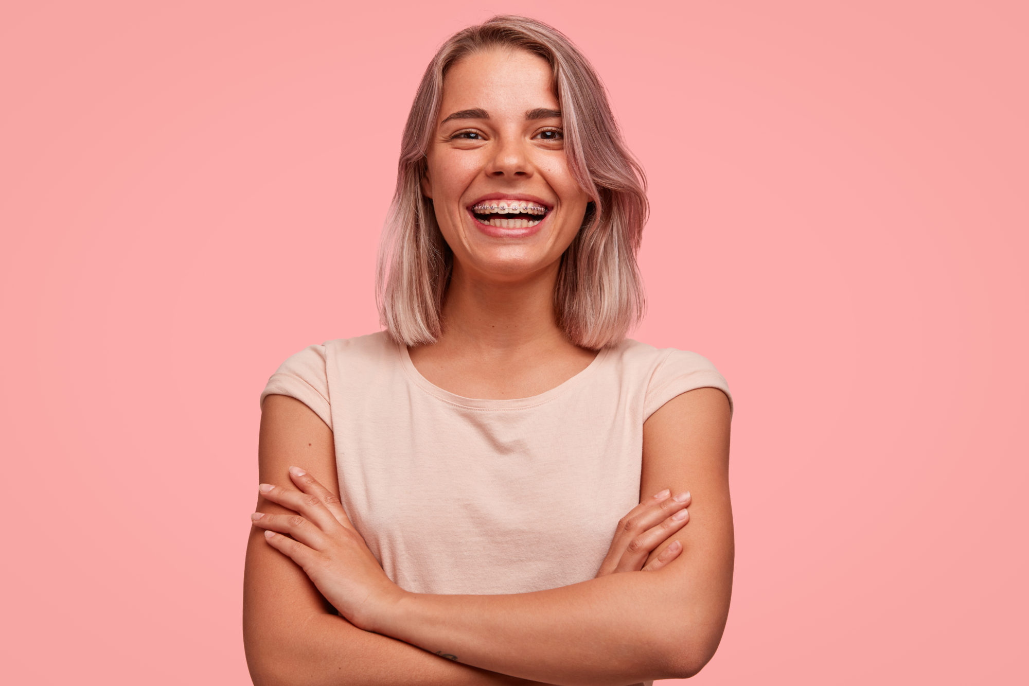 Smiling young woman with braces, showcasing a confident expression against a pink background, representing orthodontic treatment options at Braces by Dr. Ruth in Nashville.