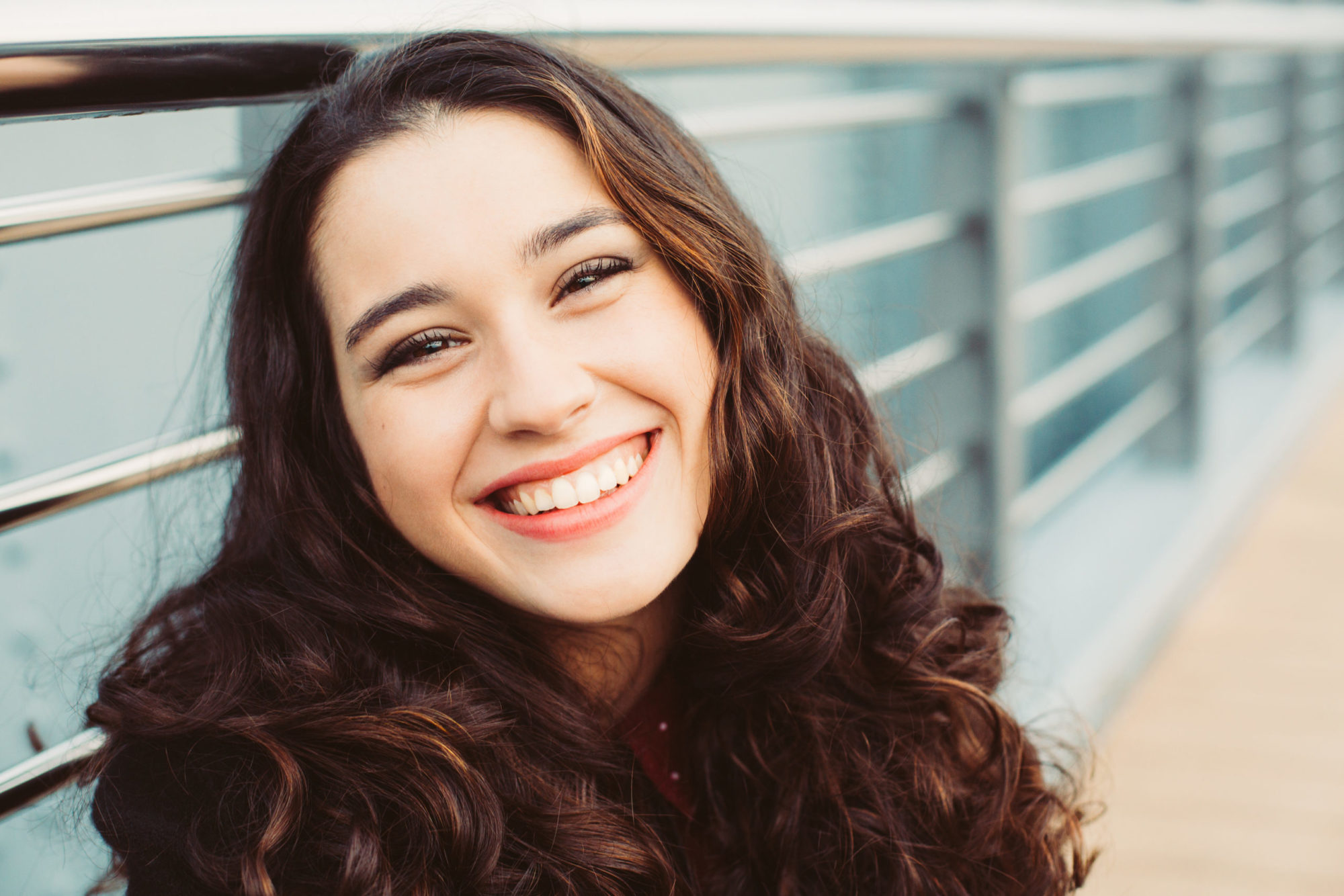 Smiling young woman with curly hair, showcasing a straightened smile, representing the benefits of Invisalign treatment at Braces by Dr. Ruth in Brentwood.