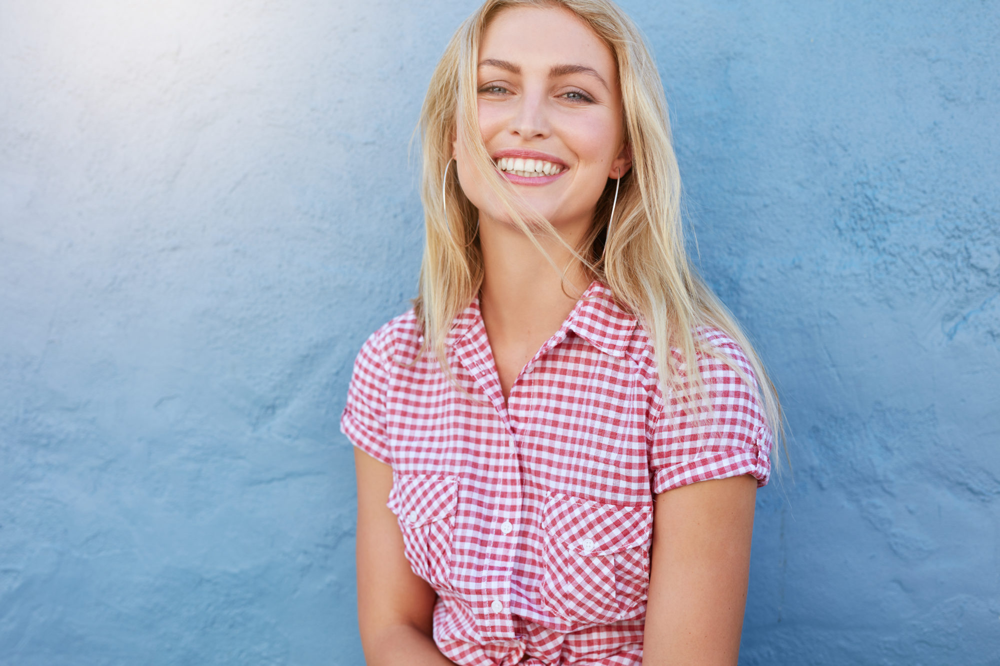Smiling young woman with straight teeth against a blue wall, representing successful Invisalign treatment at Braces by Dr. Ruth in Brentwood.