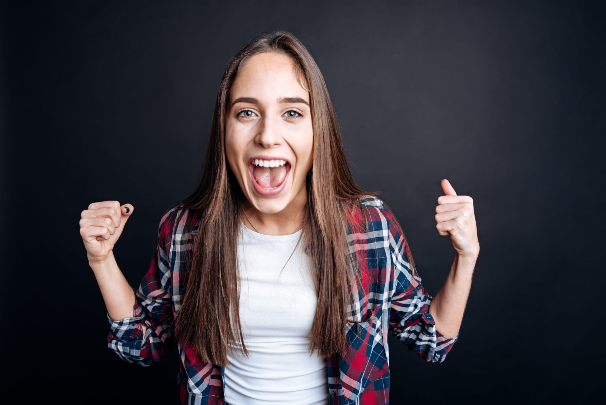 Young woman celebrating with a big smile, wearing a plaid shirt, emphasizing the joy of achieving a straighter smile with Invisalign treatment at Braces by Dr. Ruth in Brentwood.